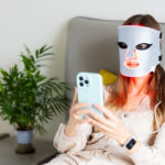 woman using led light therapy face mask and smartp 2026 05 05 19 29 19 utc